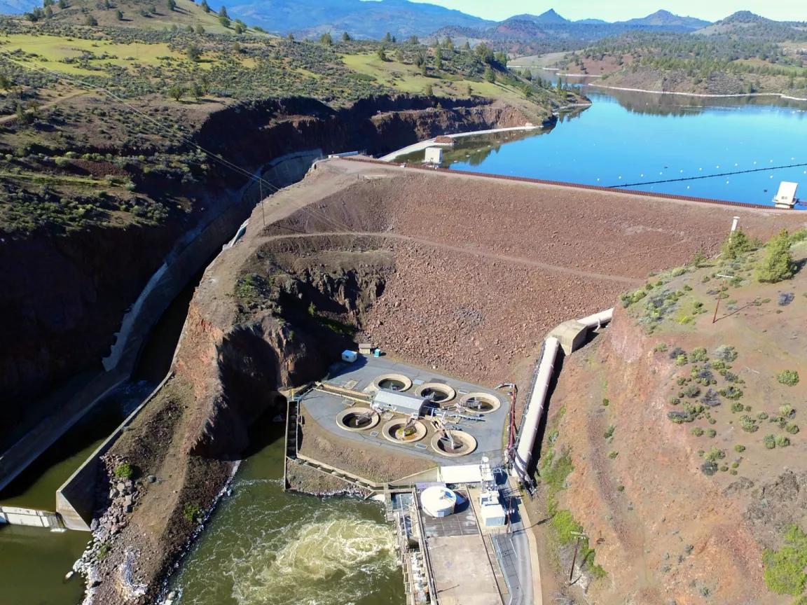 A dam facility situated in the center of a river with mountains in the background
