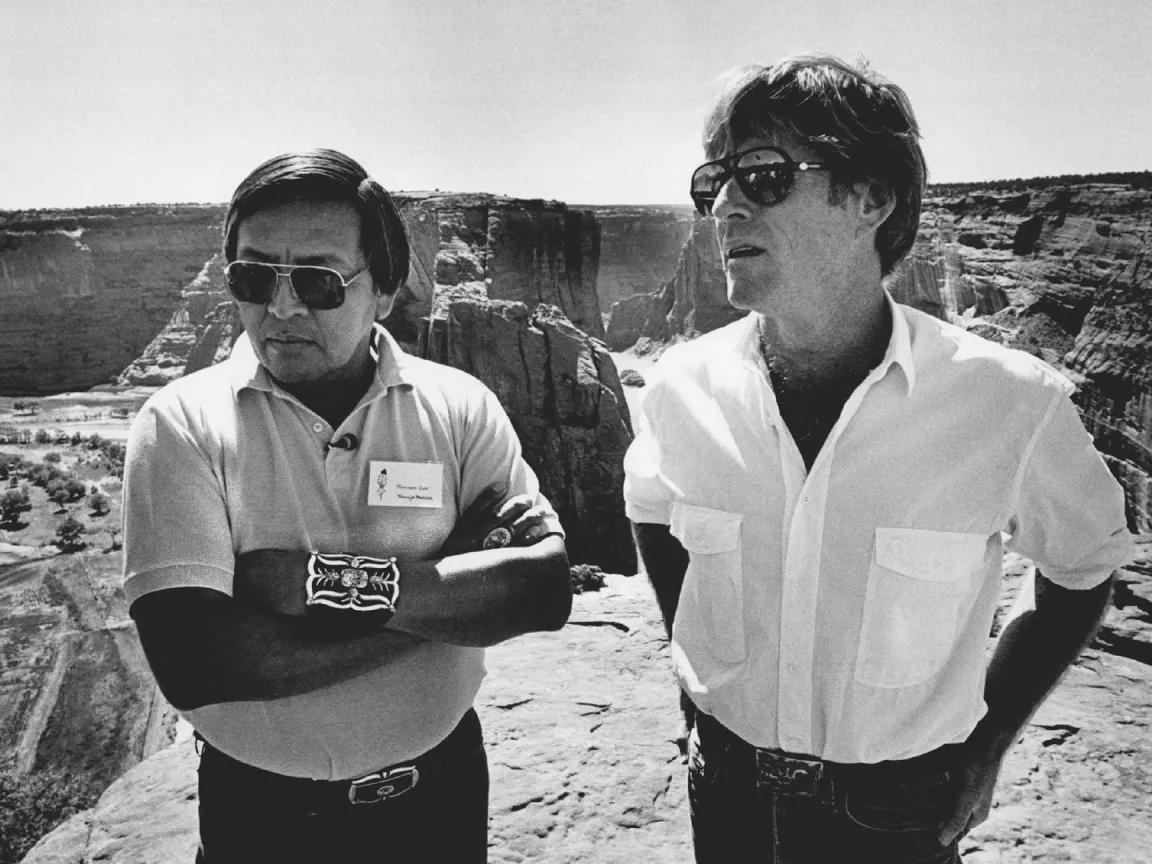 Black and white photo of Robert Redford standing next to Peterson Zah on a ledge overlooking Navajo Fortress Rock, Arizona