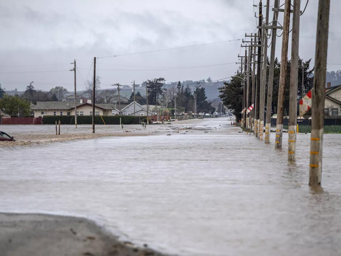 A car sinks as floodwaters flow across a road in a residential neighborhood in Monterey County, California.