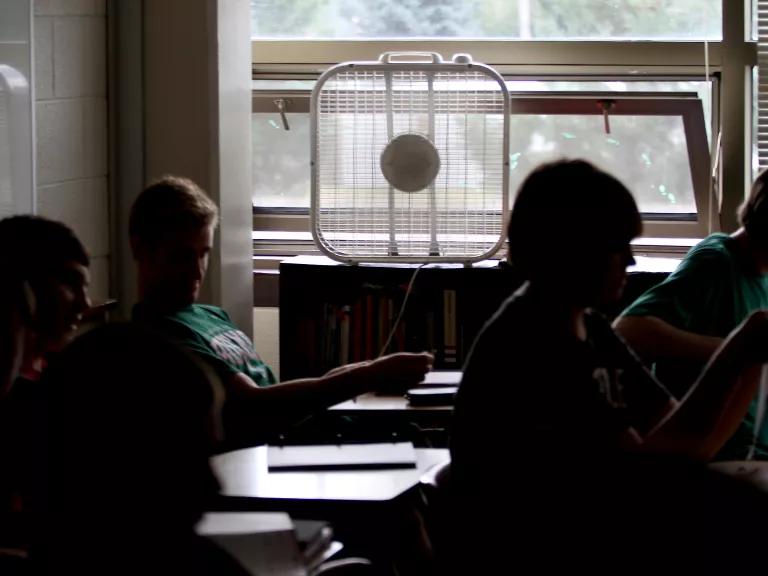 Students work in a classroom cooled by a window fan.
