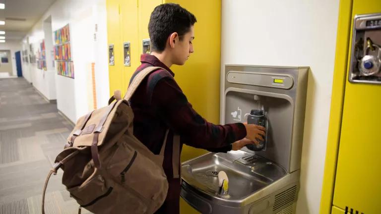 A student fills up his water bottle at a filtered drinking fountain in a school hallway.