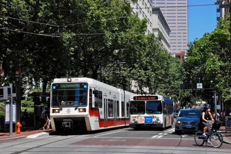 A cyclist riding past a TriMet MAX light rail train and bus stopped at the corner of 5th Ave. and Yamhill St. in Portland, Oregon