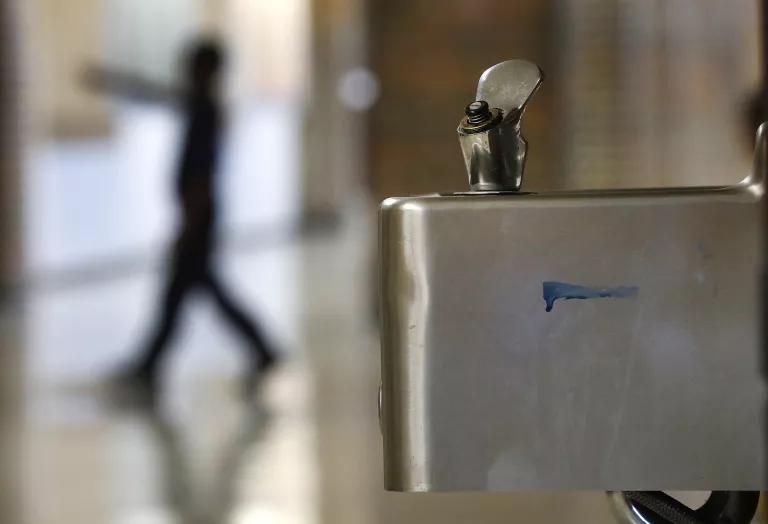 A closeup of a water fountain with a blurred image of a child walking in the background
