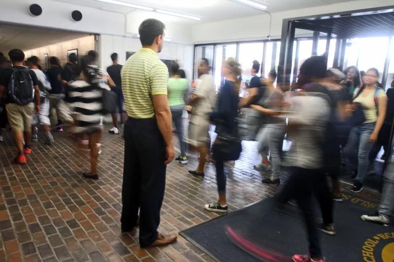 Blurred students walking through a door with a person in the middle, with their back to the camera, monitoring the students