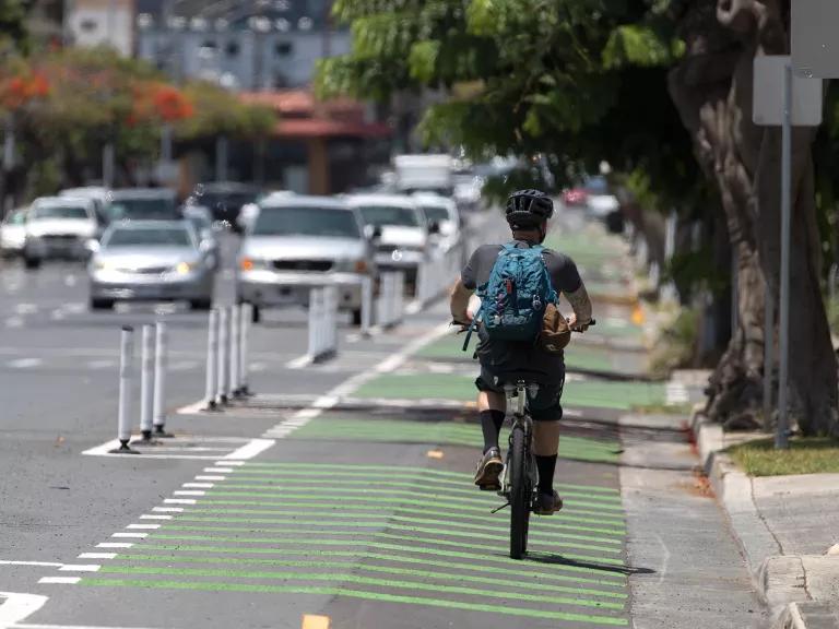 A cyclist, wearing a helmet and a backpack, rides safely in the green bike lane