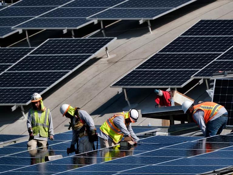 Four workers secure solar panels on a roof.