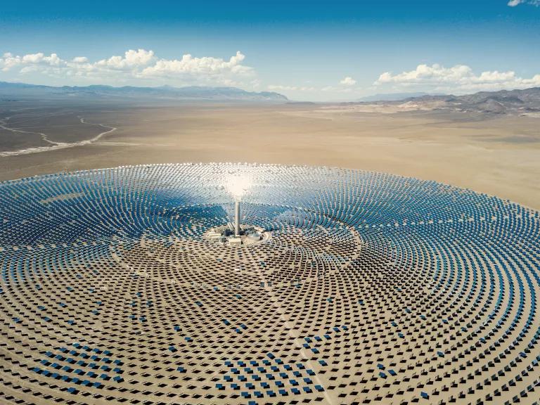 Sunlight is reflected by mirrors toward a tall receiver tower at a concentrated solar-thermal plant. 