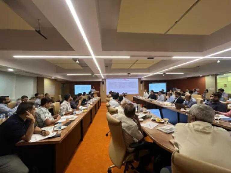 A group of people sitting around a conference tables, looking at a screen presentation
