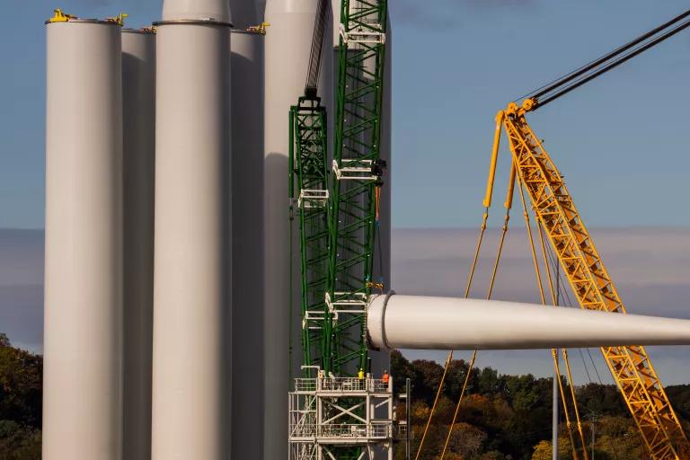 A turbine blade is lifted onto a rack near tower sections at the Revolution Wind project assembly site at State Pier in New London, Connecticut, on October 24, 2025.
