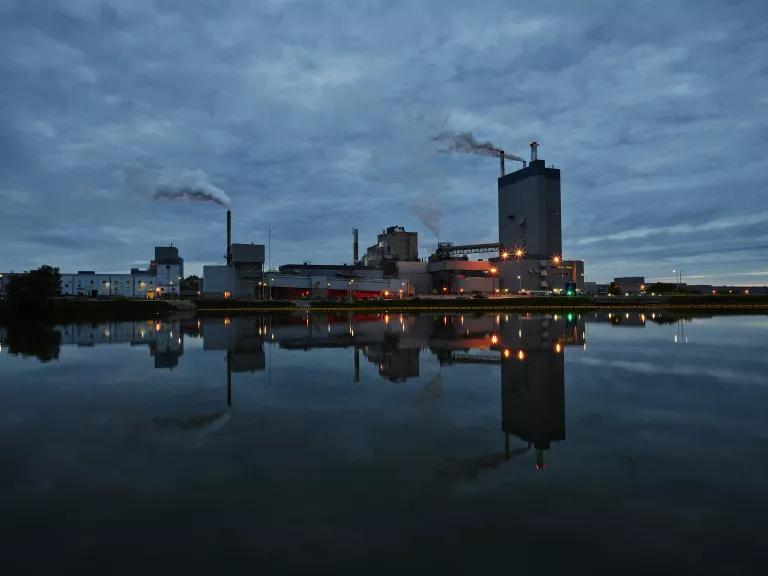 Lights shine from within an industrial facility situated next to a river at night