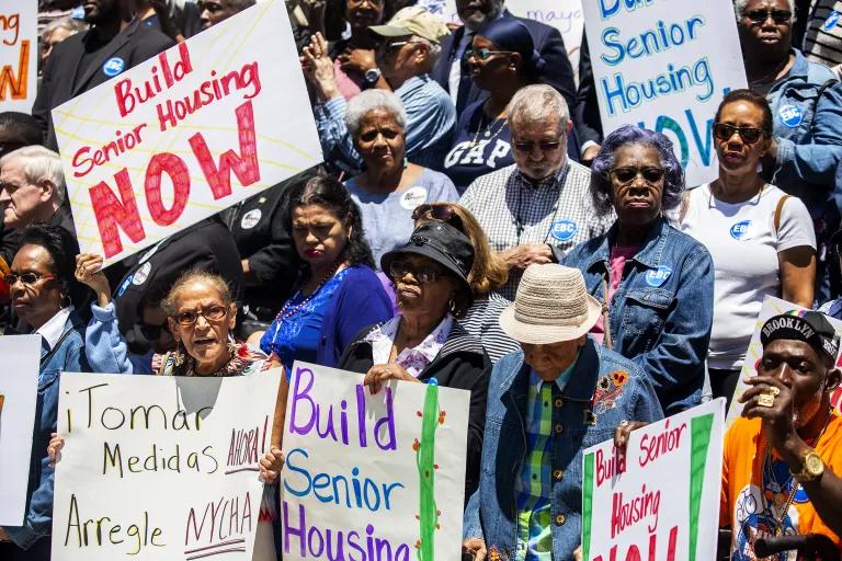 Protesters hold posters that read "Build Senior Housing Now"