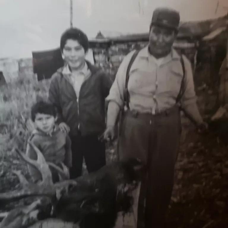 A black and white image of a man and two boys with a slaughtered reindeer