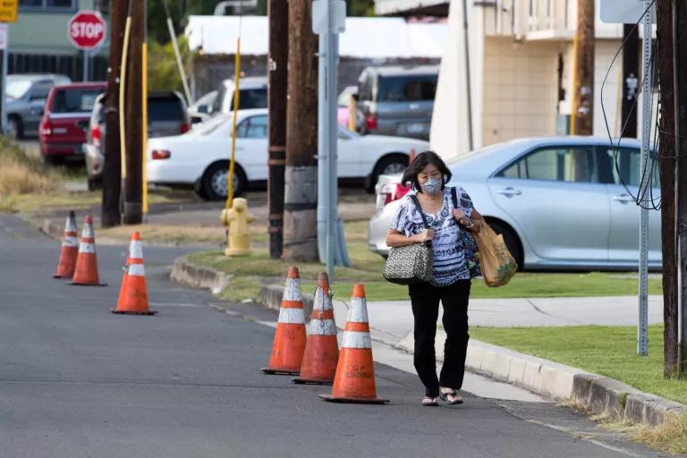 A woman walking past traffic cones that mark off a shared street where there is no existing sidewalk on Hau'oli Street in Honolulu
