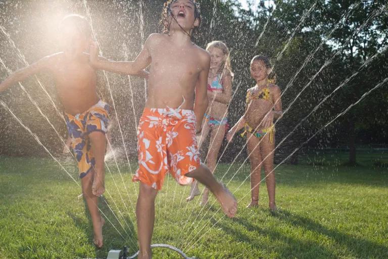Children playing in a sprinkler on a lawn