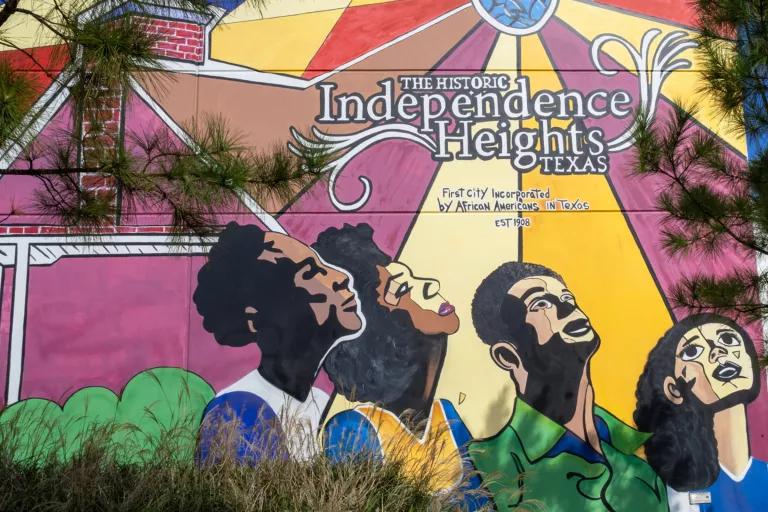 A colorful mural painted on the side of a building bears the words "The Historic Independence Heights, Texas" and depicts four people looking up toward the sky