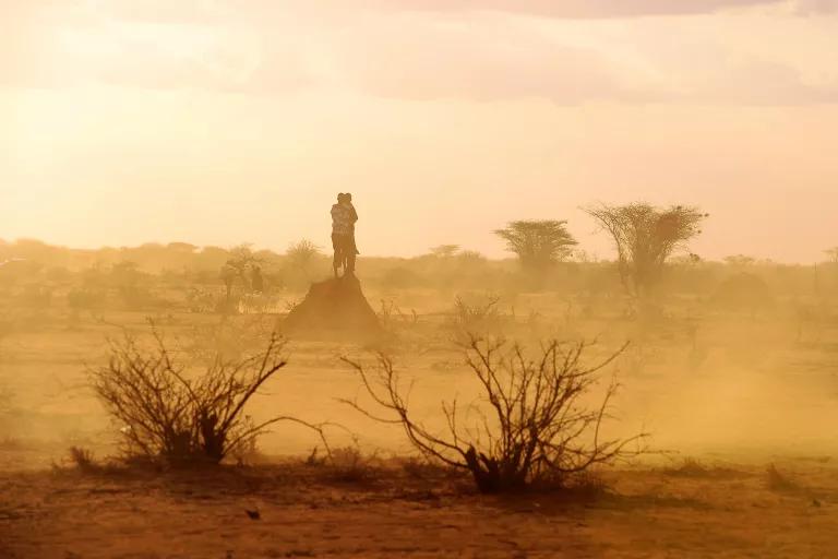 A person stands in the distance on a dry, hazy landscape