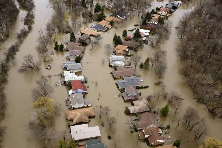 A second aerial view of two rows of single-family homes that are completely surrounded by brown floodwaters.