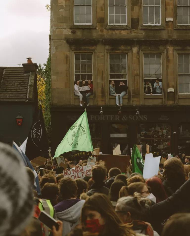 Young people with a sign that says “No Planet B” sit in a second floor windowsill overlooking a crowd of protesters in Glasgow