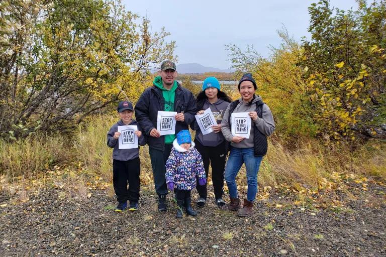 A man and woman with three children stand in front of yellow and green trees and hold signs that read "Stop the Mine"