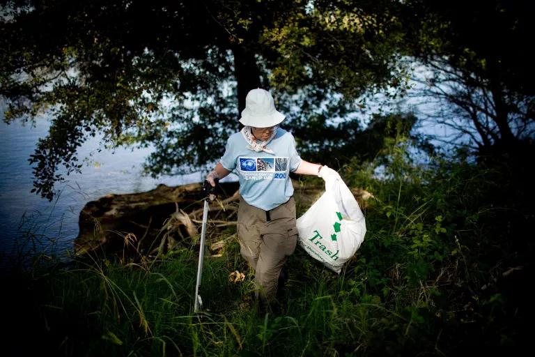 A woman wades through shallow water collecting trash
