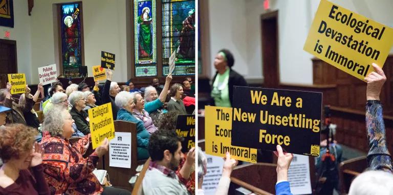 Dozens of people hold signs that read "ecological devastation is immoral" and other messages at a public meeting hosted in a church