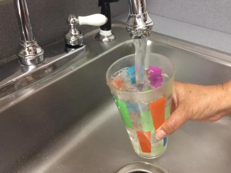 A person fills a cup with tap water from the kitchen sink