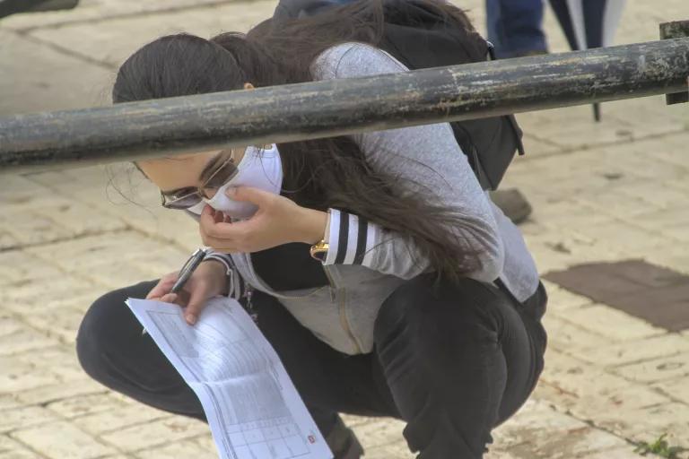 A woman crouched down near a water pipe with some documents in her hand. 