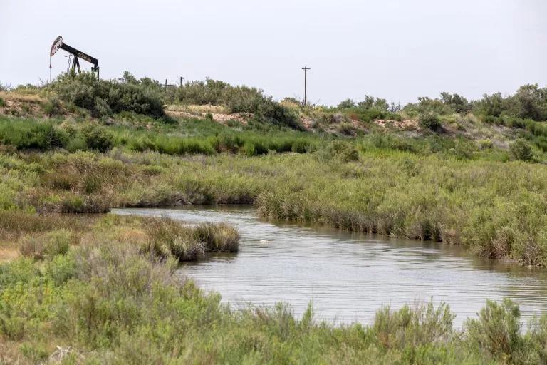 A section of river runs through a grassy area with an oil pump visible in the background
