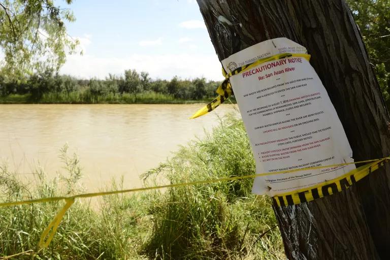 A sign posted to a tree reads in part "Precautionary Notice re: San Juan River"