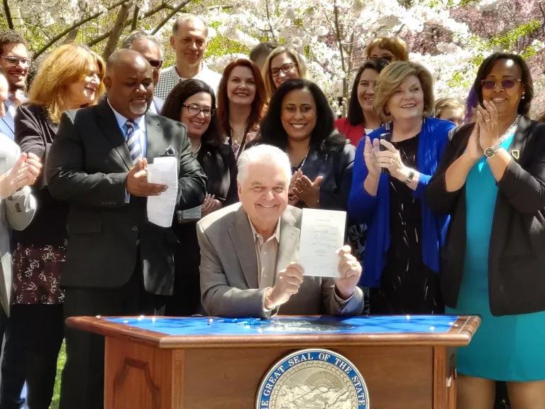 Governor Sisolak and legislators on Earth Day, holding up the signed bill supporting a stronger renewable portfolio standard, under blooming trees