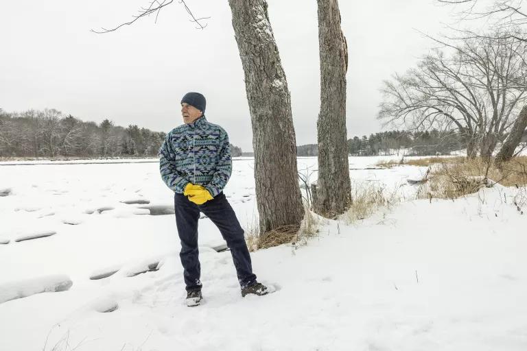 A man stands on snow-covered ground near two trees 