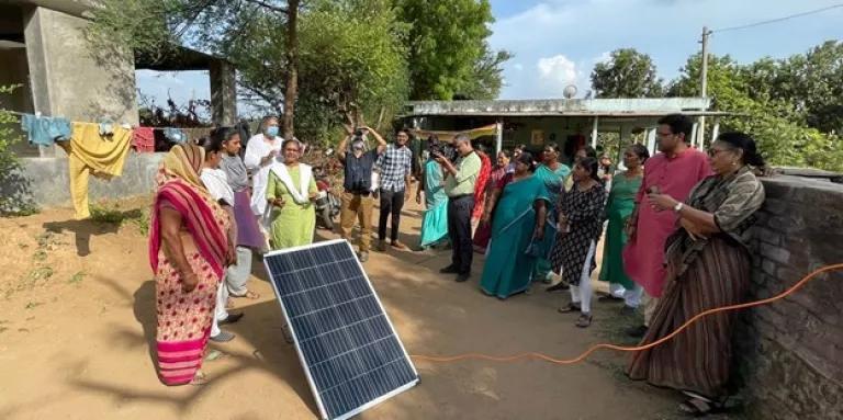 women in India stand around a solar panel discussing clean energy solutions
