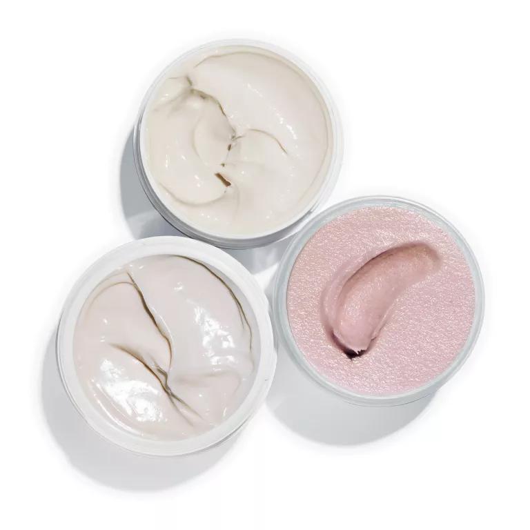 Three small jars hold white and pink creams