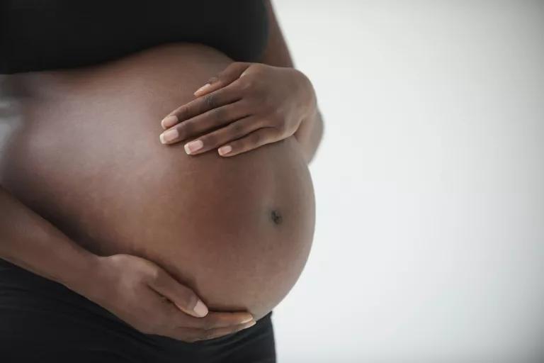 A pregnant woman's hands rest on her torso