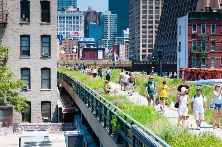 People walk along a grassy pathway built into a raised section of subway tracks over city streets
