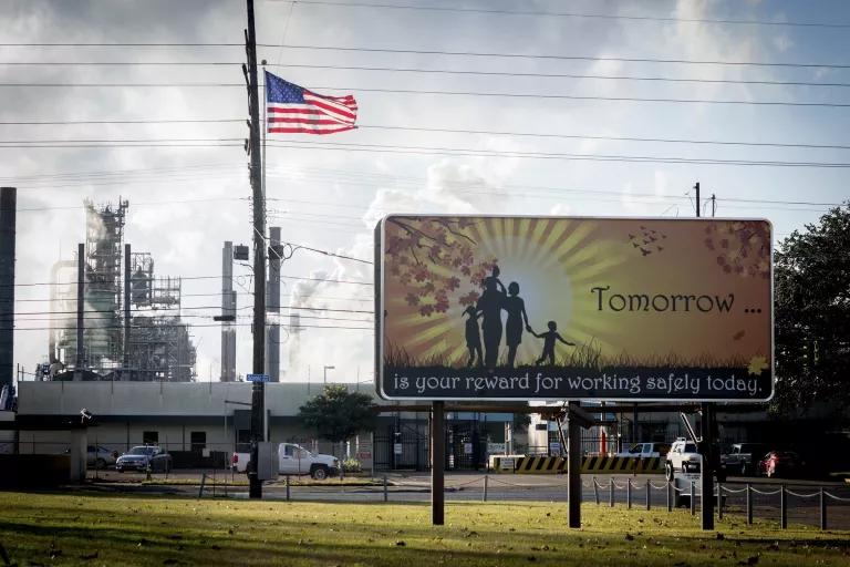 A billboard in front of an oil refinery reads "Tomorrow is your reward for working safely today"