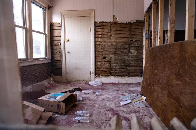 The walls of a small room are pulled down to the studs, with debris and mold visible on the floor.