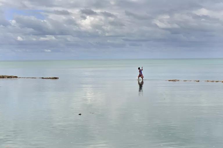 A woman walks across a sliver of land that rises just above the surface of the ocean