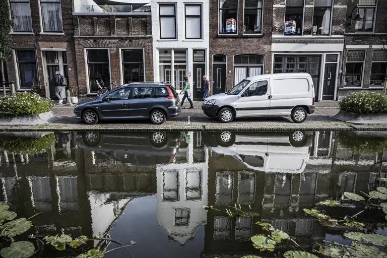 Two cars are parked in front of a row of houses, with a waterway on the other side rising almost level with the street
