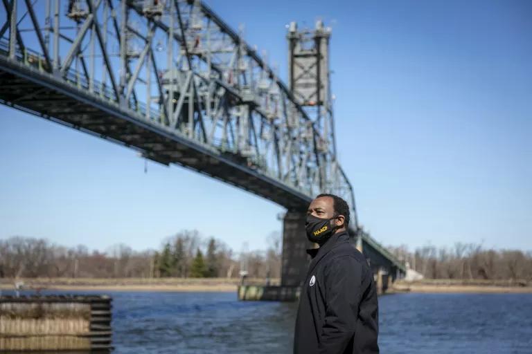 A man wearing a face mask stands under a railroad bridge