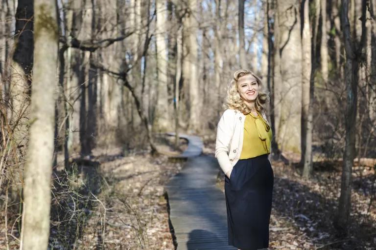 A woman stands on a pathway in a wooded area