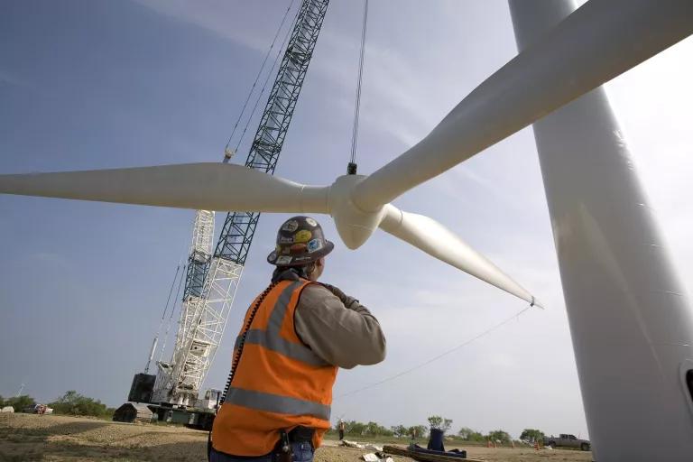 A worker stands near a wind turbine being erected