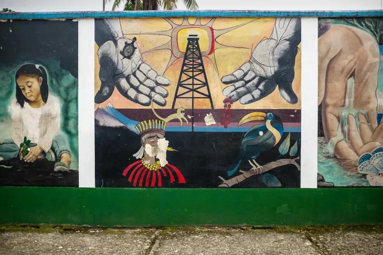 A painted mural showing an oil rig, a toucan, a child playing, and a sun with two large hands stretching out from it