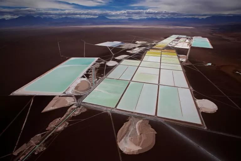An aerial view of bright bluish-green rectangualr brine pools and processing facilities on a vast expanse of land