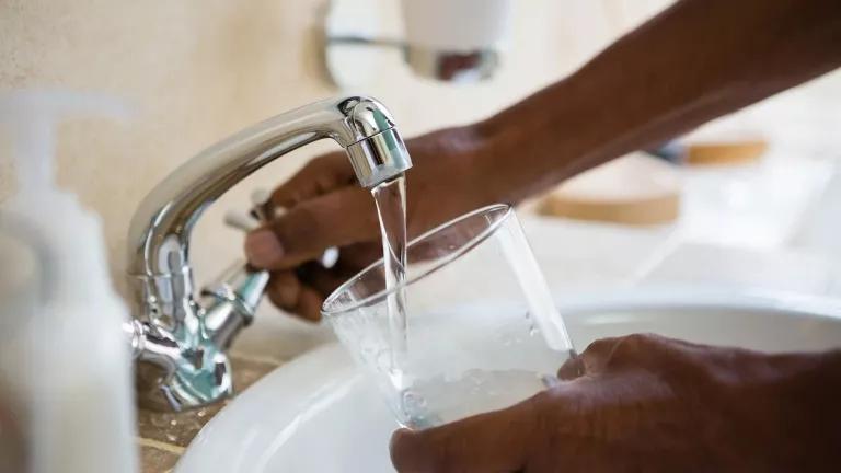Hands getting a glass of water from a faucet