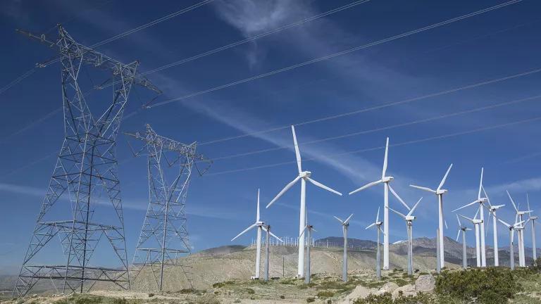 Wind turbines stand next to power lines in the California desert