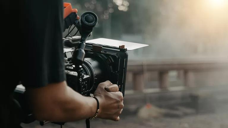 A close up of the arm of a cameraperson in a black t-shirt holding a filmmaking camera 