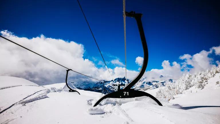 Ski lift chairs hanging from a high cable are nearly buried in snow