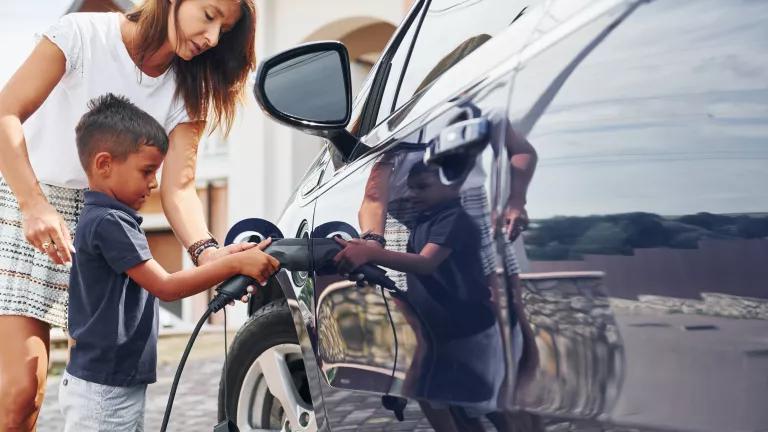 A young boy helping his mother to charge an electric car in their driveway.