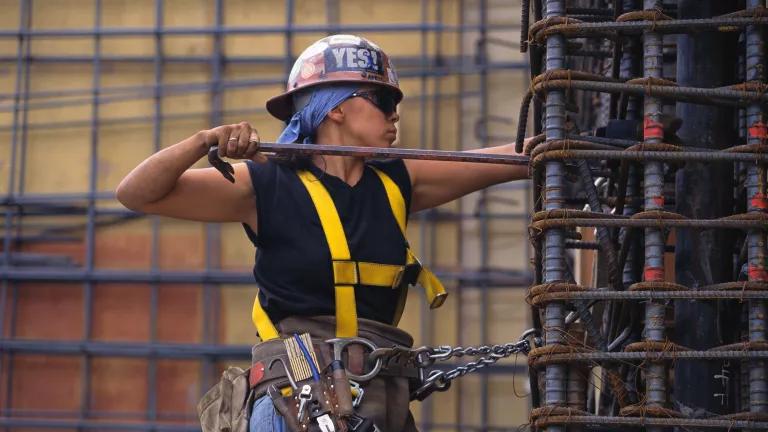 A worker bending rebar while hanging from a harness on a construction site.
